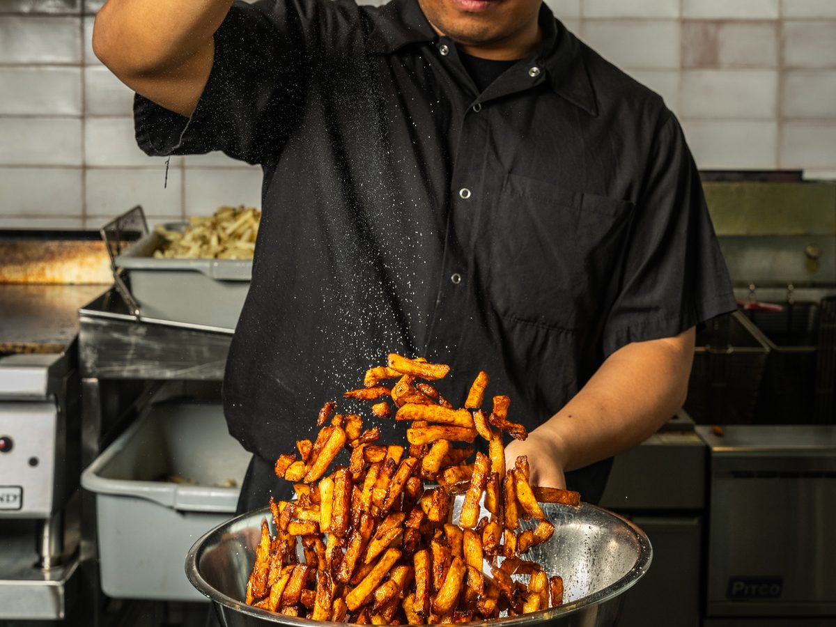 Un cuisinier de PRIME assaisonne un bol de frites fraîchement coupées dans la cuisine ouverte